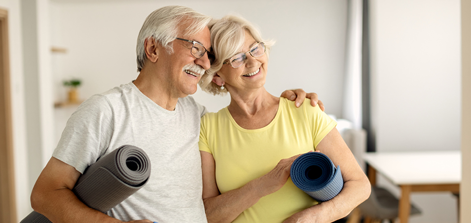 A Better Outcome for Cramping - two elderly people smiling, touching heads together and holding rolled up yoga mats.