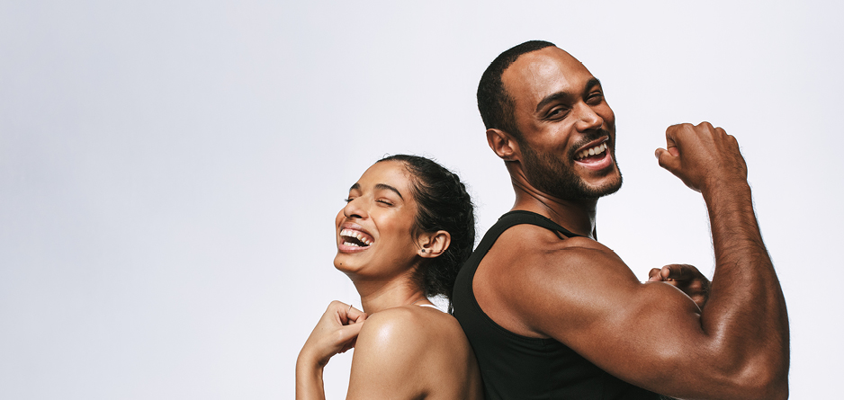Man and woman back to back, laughing and flexing their biceps muscles