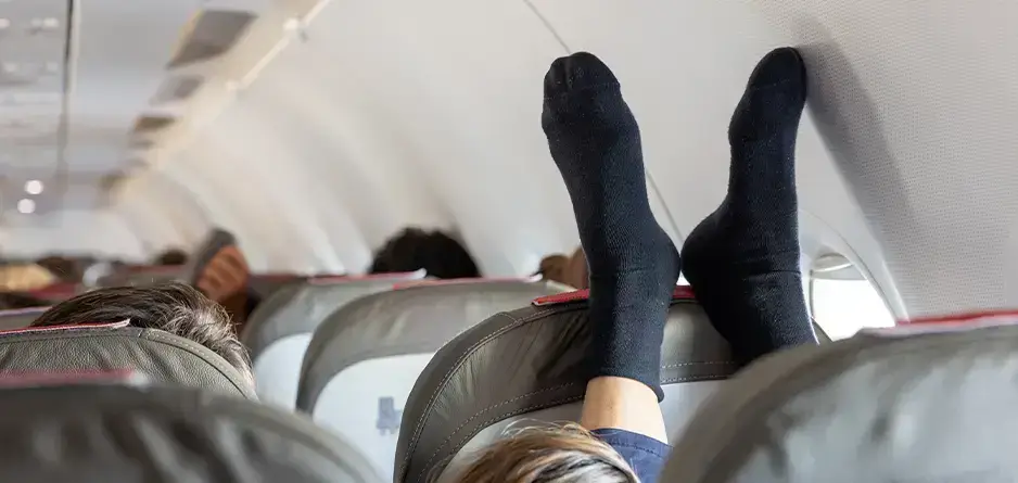 A person on a plane with their legs in the air wearing bkack socks - trying to Avoid Leg Cramps During Long Flights - using Crampeze for Leg Cramp Relief