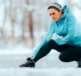 A runner in the snow holding her leg in pain due to leg cramps